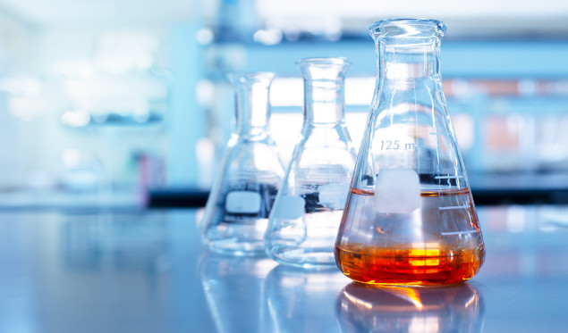 orange solution in science glass flask in blue chemistry school laboratory background
